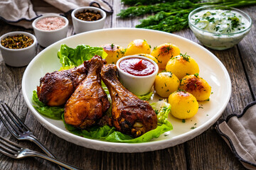 Barbecue chicken drumsticks with fried potatoes, lettuce and ketchup on wooden table

