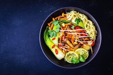 Asian food - Chow Mein noodles, stir fried vegetables, soy sauce and shimeji mushrooms on wooden table
