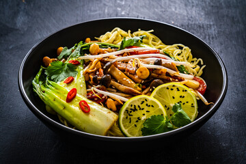 Asian food - Chow Mein noodles, stir fried vegetables, soy sauce and shimeji mushrooms on wooden table
