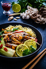 Asian food - Chow Mein noodles, stir fried vegetables, soy sauce and shimeji mushrooms on wooden table
