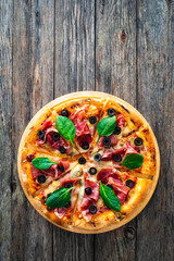 Circle prosciutto pizza with mozzarella, black olives and spinach leaves on wooden table
