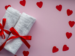 Flat lay with a lot of tiny heart-shaped papers, two towels and space for text. Red heart paper background with towels tied with a red bows. Valentines day spa, bath, self care and body care concept.