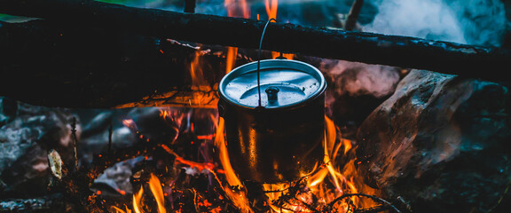 Kettle in soot hanging over fire. Cooking food at fire in wild. Beautiful firewoods burn in bonfire close-up. Survival in wild nature. Wonderful flame with caldron. Pot hangs in campfire flames.