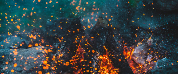 Vivid smoldered firewoods burned in fire closeup. Atmospheric background with orange flame of campfire. Full frame image of bonfire with sparks in bokeh. Warm vortex of glowing embers and ashes in air