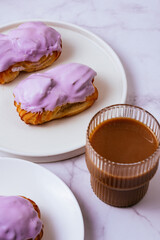 eclair in purple berry glaze and coffee with milk in a glass