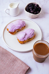 eclair in purple berry glaze and coffee with milk in a glass