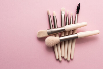 Set of makeup brushes on soft pink colored background. Top view, flat lay.