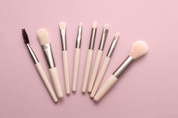 Set of makeup brushes on soft pink colored background. Top view, flat lay.