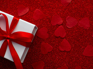 White gift box is on red heart paper background, top view. Greeting card, present. Valentines day holiday concept. Flat lay with a lot of tiny heart-shaped papers with space for text. February 14th.