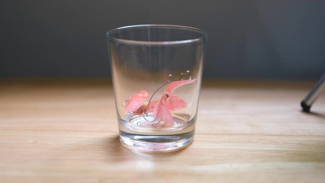 Man's hand puts retainer in glass of water and pours water for soaking or rinsing.