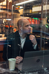 man young businessman entrepreneur caucasian,seriously enthusiast, bald in suit, sitting at a table, working laptop, talking via phone, remote job, in cafe window .concept entrepreneur lunch .