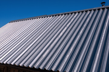 Metal roof constructed from galvanized iron sheets on the background of the blue sky; roof of a house in the countryside