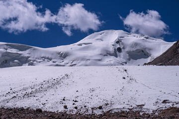 Snow - ice peak with powerful glaciation against a blue sky with clouds