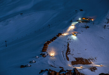Ski base in the evening during the winter season; work of snow plows to level the main ski run
