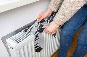 The woman's hand takes dried warm socks after washing on a heating radiator at home.