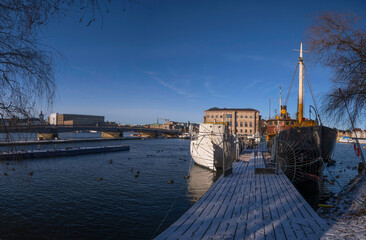 Moored fishing boat and a steam pilot boat at a snowy wood pier a winter day in Stockholm