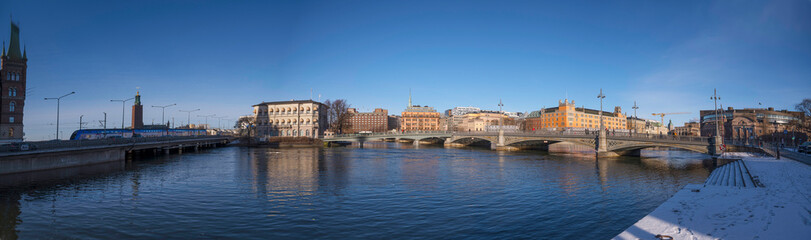 Fototapeta na wymiar Panorama. The Town City Hall, government and department buildings. The bridge Vasabron and the high way Söderleden passing over the river Strömmen a sunny snowy winter day in Stockholm