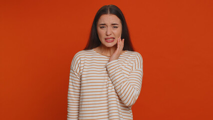 Hipster pretty woman touching sore cheek suffering from toothache cavities or gingivitis waiting for dentist appointment gums disease. Young girl indoor studio shot isolated alone on red background