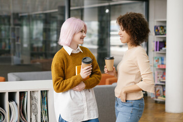 African American and Caucasian women colleagues in office enjoy friendly warm conversation, multi-ethnic mates having informal talk drink coffee, take break