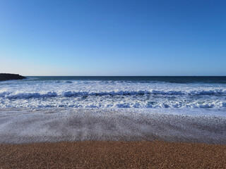 Praia com algumas ondas num dia ensolarado com um bonito céu azul - obrazy, fototapety, plakaty