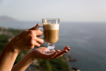 Glass mug with coffee at sunset in female hands. Close-up.