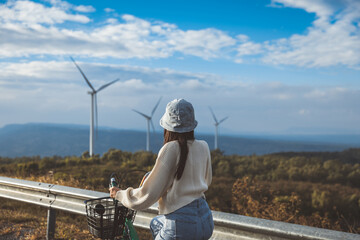 Asian woman traveler with bicycle relax and travel with wind turbine on mountain background Thailand