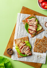 Healthy food concept. Snack crispbread toast with seeds, baked meat with tomatoes and salad on a cutting board on a light green background. View from above.