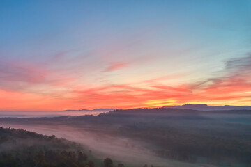 Foggy landscape at sunrise. Range of hills in front of agricultural fields. Blue sky with red accents. Fog in the valley in the autumn season. Aerial view with drone. Germany, Nurtingen, Swabian alb.