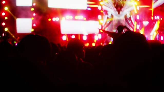 People clap their hands and dance at evening concert with light show.Fans raise their hands in bright colorful strobe lights on stage. Crowd is dancing, filming performance rock band, throwing party.