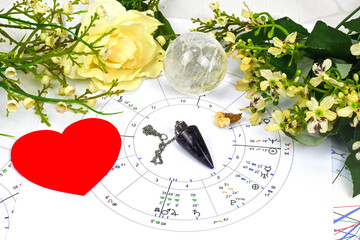 Printed astrology birth chart and white flowers, heart, pendulum and clear quartz crystal spheres,...