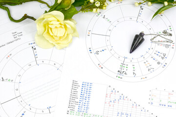 Printed astrology birth chart and white flowers and pendulum , workplace of astrology, spiritual,...