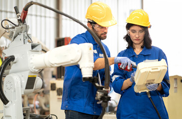 Female industrial engineer using remote control board to check robotic welder operation in modern automation factory. Maintenance technician monitoring robot controller for automated steel welding.