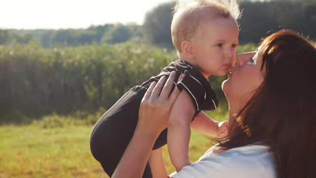 mom kiss newborn baby son holds in his arms playing in the park. mother day kid dream childhood happy family concept. parent play on hands with a lifestyle little boy son sunlight. people in the park