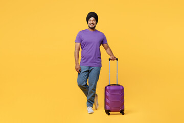 Traveler Sikh Indian man ties his traditional turban dastar wear t-shirt holding bag isolated on plain yellow background Tourist travel in free spare time rest getaway Air flight trip journey concept