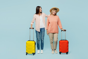 Elder parent mom with young adult daughter two women in casual clothes hat hold suitcase bag isolated on plain blue background Tourist travel abroad in free time rest getaway Air flight trip concept