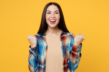 Young excited fun caucasian woman wear blue shirt beige t-shirt doing winner gesture celebrate clenching fists say yes isolated on plain yellow background studio portrait. People lifestyle concept.