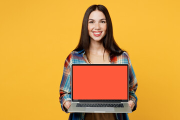 Naklejka premium Young cheerful fun smart smiling IT woman wearing blue shirt beige t-shirt hold use working on laptop pc computer with blank screen workspace area isolated on plain yellow background studio portrait.