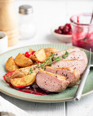 Duck breast with potatoes and berry sauce on wooden background, selective focus