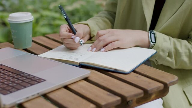 Close-up image on manicured details of a nude woman typing beautifully on the keyboard of a modern computer. Dressed classically, she notes with a pen in the diary in the park. Work concept
