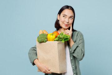 Fototapeta na wymiar Young woman wear casual clothes hold brown paper bag with food products put hand prop up on chin look aside isolated on plain blue background studio portrait. Delivery service from shop or restaurant.