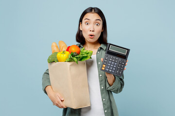 Fototapeta na wymiar Young shocked confused woman in casual clothes hold brown paper bag with food products show calculator isolated on plain blue cyan background studio portrait Delivery service from shop or restaurant