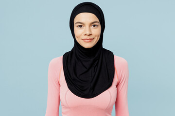 Young smiling fun arabian asian muslim fitness trainer sporty woman wear pink abaya hijab spend time in home gym looking camera isolated on plain blue background studio. Workout sport fit abs concept.