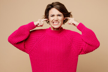 Young sad irritated woman wear pink sweater closed eyes cover ears with hands fingers do not want...