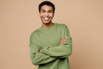 Young smiling man of African American ethnicity wear green sweatshirt look camera hold hands crossed folded isolated on plain pastel light beige background studio portrait. People lifestyle concept.