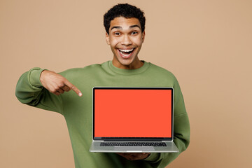 Young excited IT man of African American ethnicity wears green sweatshirt hold use work on laptop pc computer with blank screen workspace area isolated on plain pastel light beige background studio.