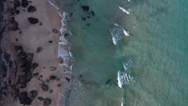 Aerial top view of sea waves crashing on the shoreline in Fuerteventura - top view with 4k drone at sunset