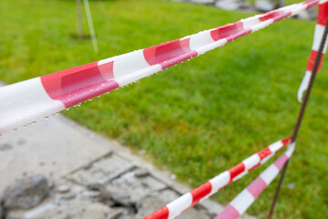 Striped restraining tape blocks the passage before road repair work in the public park