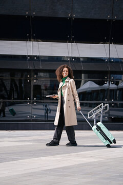 Young african woman walking outdoors carrying a suitcase and going to travel by airplane at modern airport. Vacations, travel and active lifestyle concept     