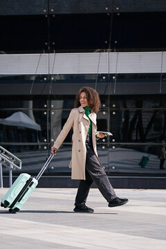 Portrait young african woman walking outdoors carrying a suitcase and going to travel by airplane at modern airport. Vacations, travel and active lifestyle concept   