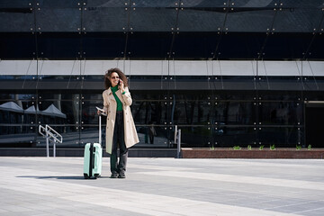Young african woman walking outdoors carrying a suitcase and going to travel by airplane at modern airport. Vacations, travel and active lifestyle concept     